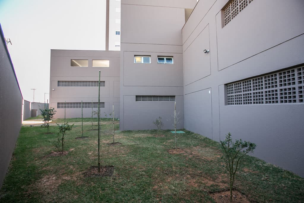 Fachada lateral de edifício residencial com jardim e gramado em fase de crescimento.