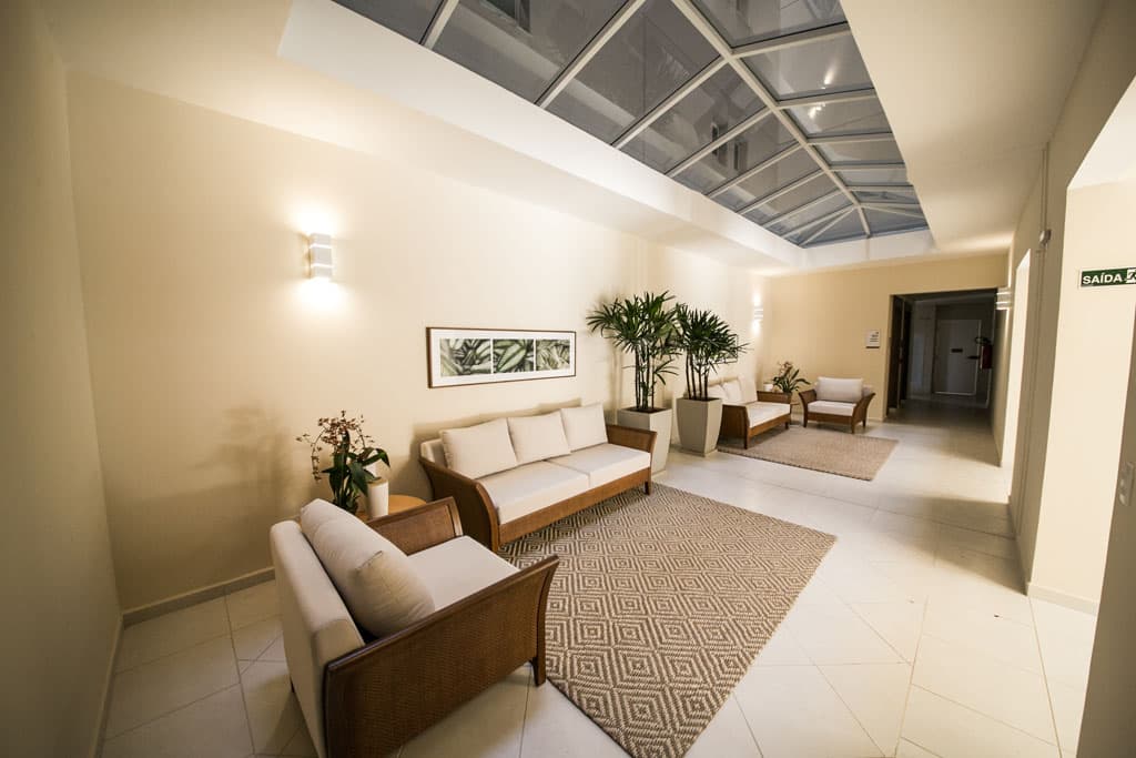 Lounge de recepção com teto de vidro retrátil, sofás em tons claros e tapetes geométricos.