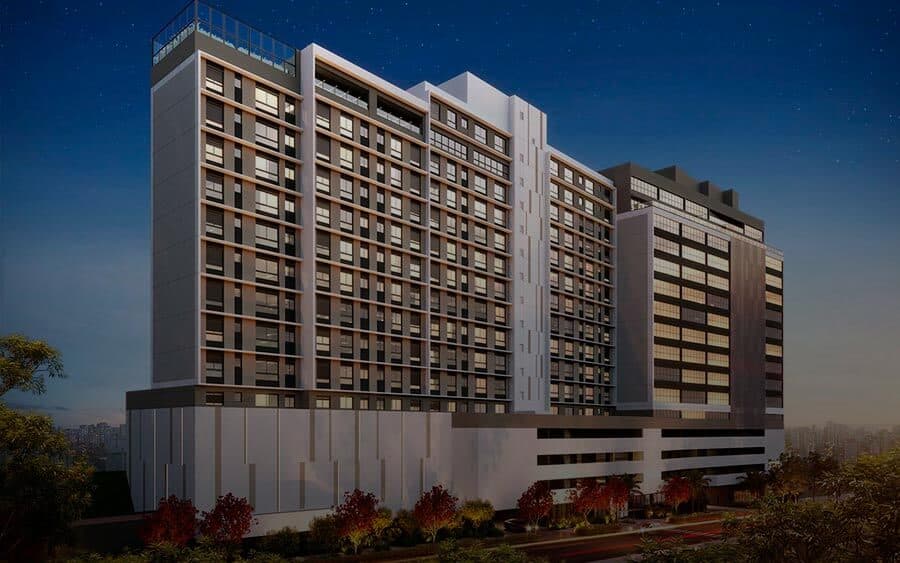 Fachada noturna de edifício residencial de múltiplos andares com iluminação nas janelas.