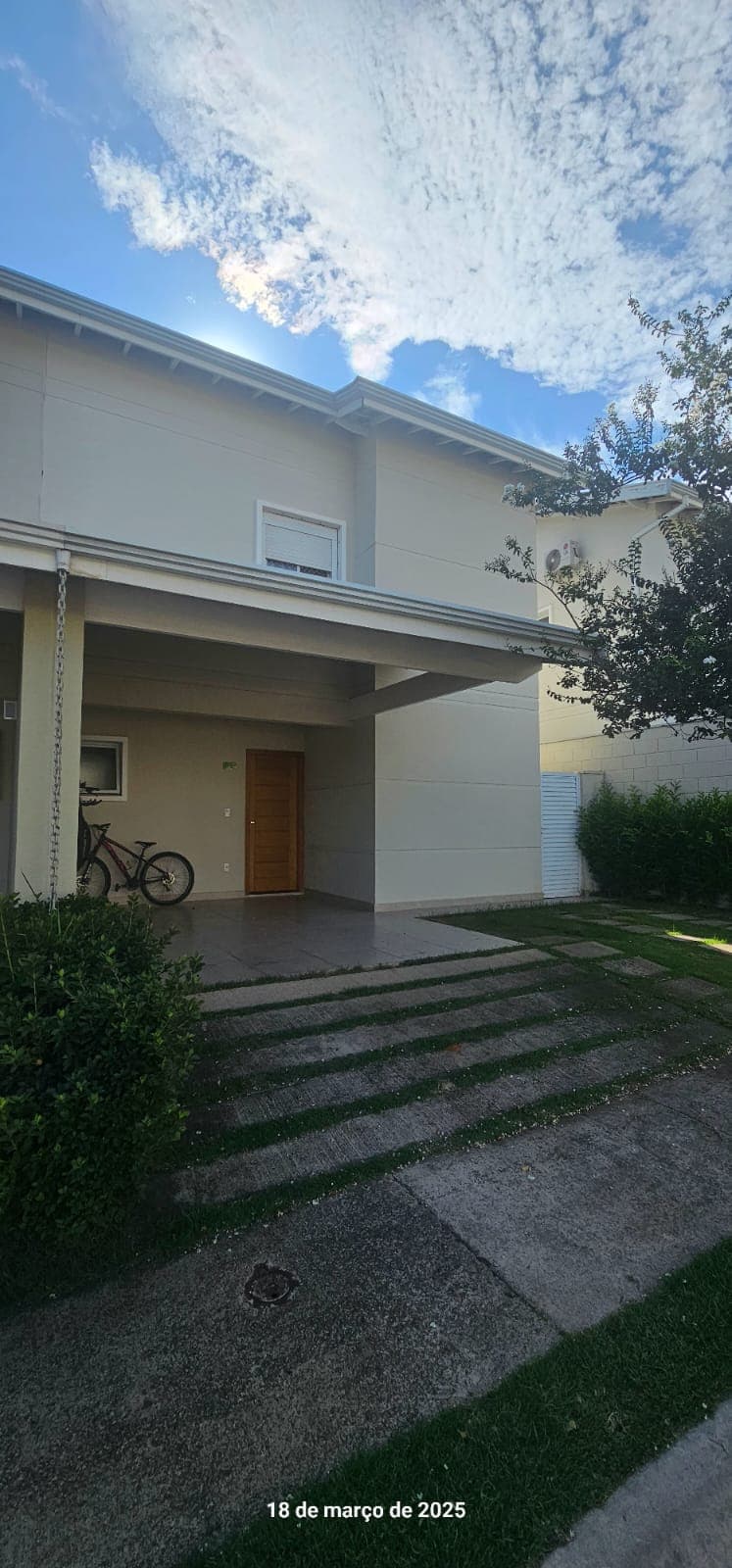 Fachada da casa com garagem coberta, porta de madeira e jardim frontal